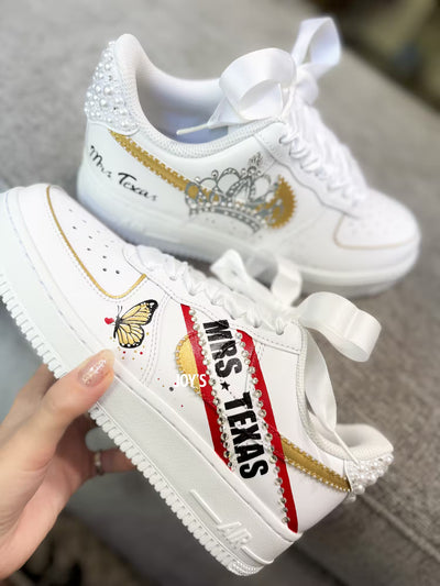 White custom wedding sneakers with pearl-embellished heel, rhinestone details, red and blue painted accents, and personalized “Mrs. Texas” text on the side, shown in a close-up side view