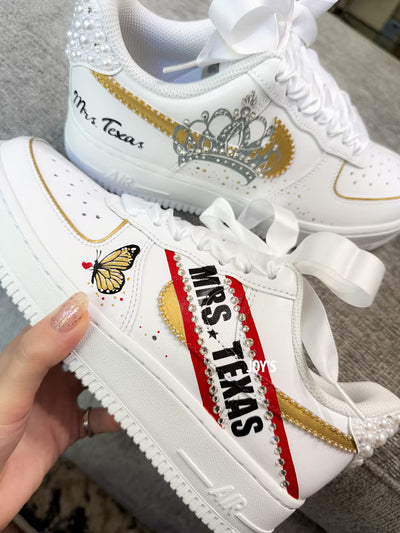 White custom wedding sneakers with pearl-embellished heel, rhinestone details, red and blue painted accents, and personalized “Mrs. Texas” text on the side, shown in a close-up side view