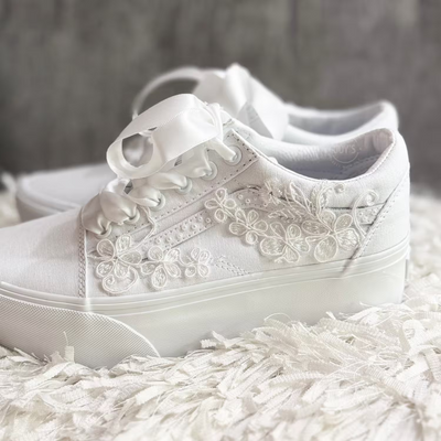 White platform Vans wedding sneakers with lace floral appliqués, pearl detailing, and satin ribbon laces, shown in a close-up side view
