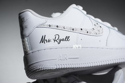 White Nike Air Force 1 sneaker with rhinestone embellishments on the Swoosh, custom black script reading 'Mrs. Ryall' on the side, and a white sole with 'AIR' embossed.