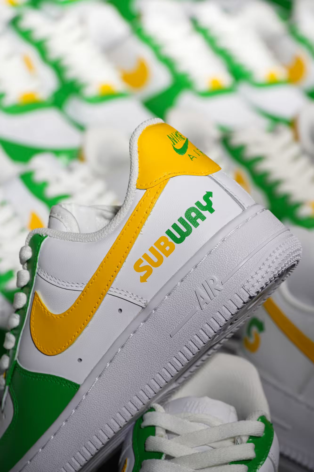 White sneaker with yellow and green accents featuring the 'Subway' logo on a blurred background.