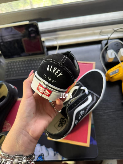Black Vans custom wedding sneakers with wedding date printed on the heels, shown in a rear view on a Vans shoebox