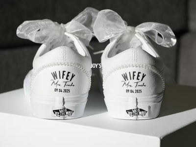 White Vans sneakers with 'Wifey' text, tied with ribbons and pearls on a white surface.