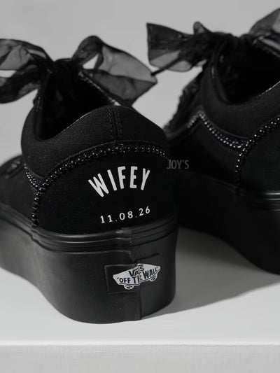 Black platform Vans custom wedding sneakers with pearl trim, satin ribbon laces, and “Wifey” text with wedding date printed on the heel, shown in a close-up rear view