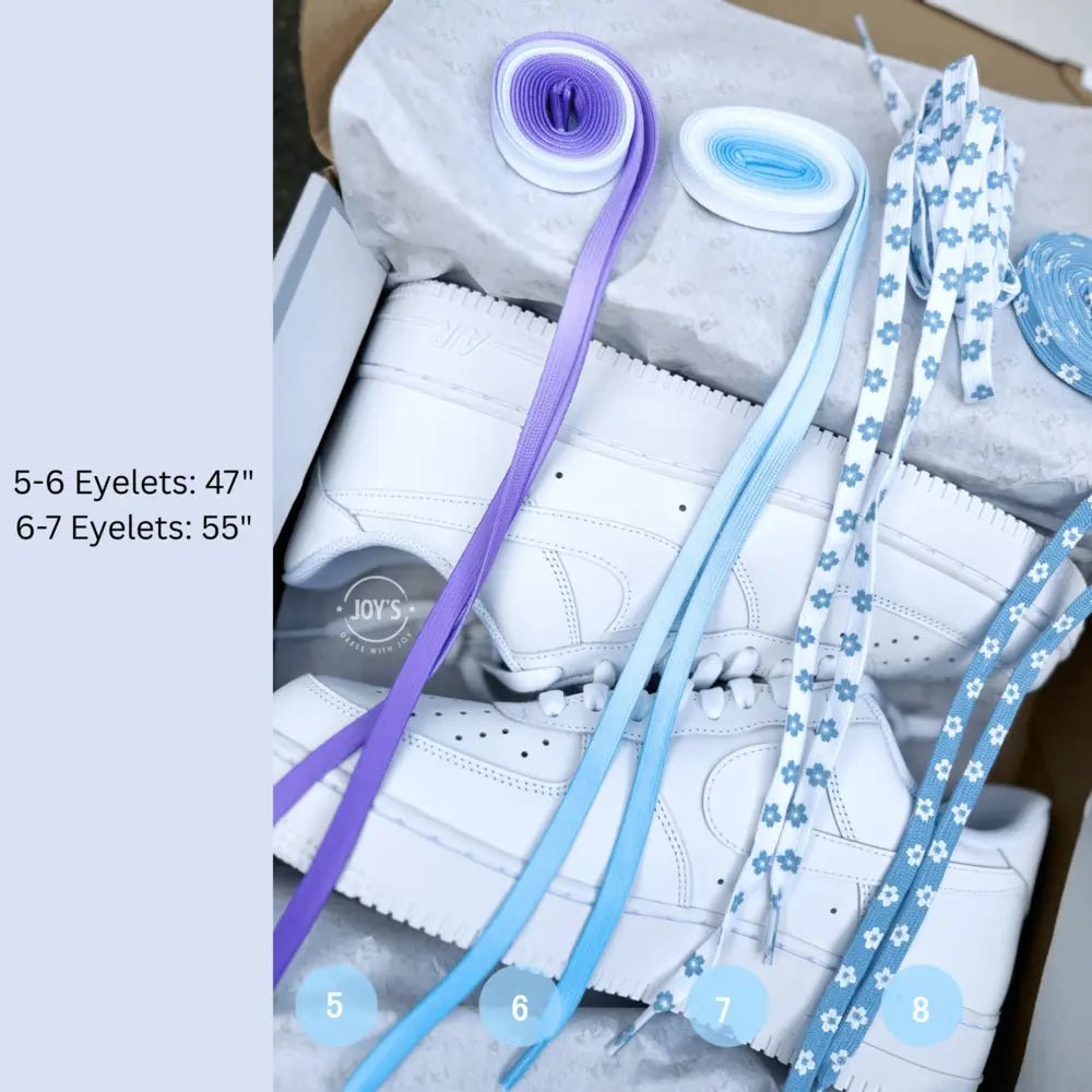 Assorted sneaker laces laid out in a box, including purple, light blue, and blue floral-pattern laces, shown rolled and extended to display length and style options.