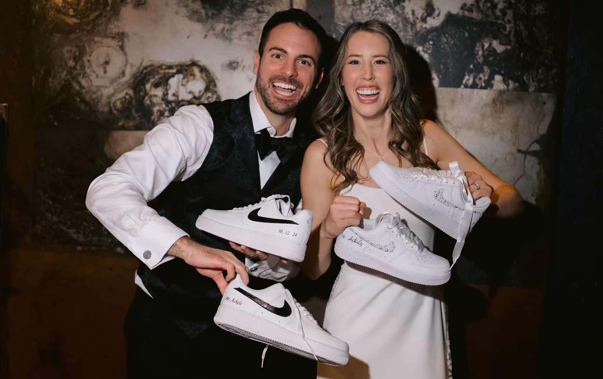 Bride and groom holding custom white Nike sneakers with wedding date personalization.