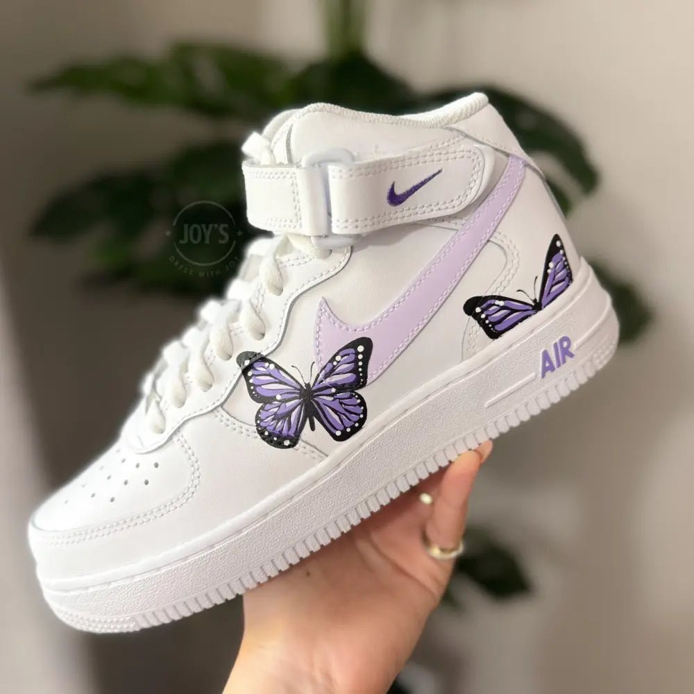 Custom white Nike Air Force 1 Mid Sneakers with hand-painted purple butterfly artwork and soft lilac swoosh.