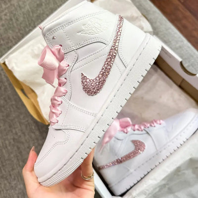 White Nike Air Force 1 Mid sneakers (standard sole, not platform), customized with a blush-pink crystal swoosh and matching pink ribbon laces. Clean, elegant finish with a soft bridal vibe, keeping the classic AF1 profile while adding subtle sparkle.