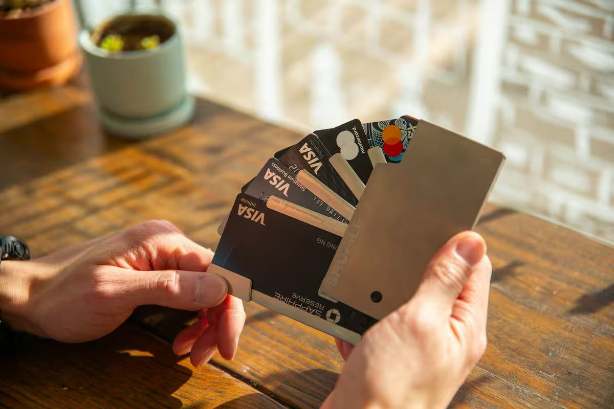 Person holding a set of credit cards on a wooden table with a blurred background