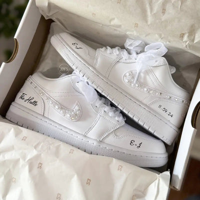 White Nike Air Force 1 Low sneakers (standard sole, not platform), customized with a crystal-embellished swoosh and subtle rhinestone detailing along the panels. Finished with sheer white ribbon laces and personalized black script on the heel and toe, giving a clean, elegant bridal look.
