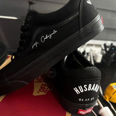 Black Vans custom wedding sneakers with “Husband and wedding date printed on the heels, shown in a rear view on a Vans shoebox