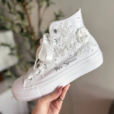 White platform Vans wedding sneakers with lace floral appliqués, satin ribbon laces, and personalized bride name printed on the side, shown in a close-up angled view