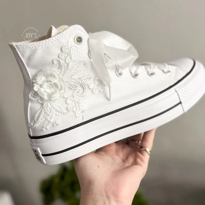 White platform Converse Chuck Taylor wedding sneakers with lace floral appliqués, satin ribbon laces, and personalized initials printed on the side, shown in a clean studio side view
