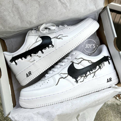 White Nike Air Force 1 with black drip swoosh design and subtle lightning accents, shown inside the shoebox.