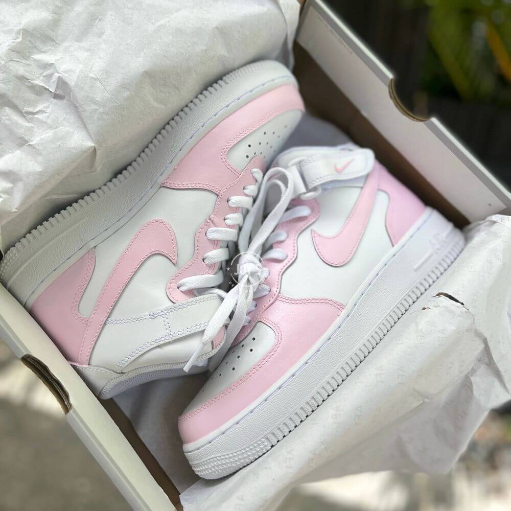 White Nike Air Force 1 Mid-top sneakers with soft pink panels and swoosh, displayed in a white box