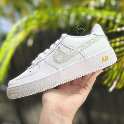 White Nike Air Force 1 with light gray swoosh accented by small yellow floral details, shown from the side.