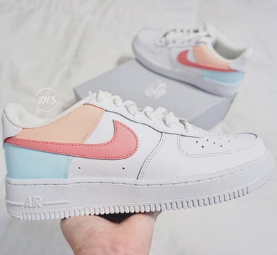 Custom Nike Air Force 1 low sneakers with pastel color block design, featuring coral pink swoosh, peach heel panel, and light blue rear panel on a white leather base.